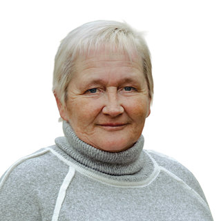 Eine ältere Frau mit kurzen, grauen Haaren steht lächelnd vor einem neutralen Hintergrund. Sie trägt einen grauen Pullover mit hohem Kragen. Ihr Ausdruck wirkt freundlich und einladend.