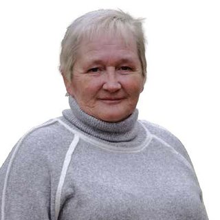 Ein lächelnde ältere Frau mit kurzen, grauen Haaren trägt einen hellgrauen Pullover mit Stehkragen. Der Hintergrund ist einfarbig.