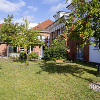 Ein ruhiger Innenhof mit Rasenfläche und mehreren kleinen Bäumen. Im Hintergrund sind zwei Gebäude mit roten Ziegelfassaden sichtbar. Die Atmosphäre wirkt freundlich und einladend, ideal für entspannte Aufenthalte im Freien.