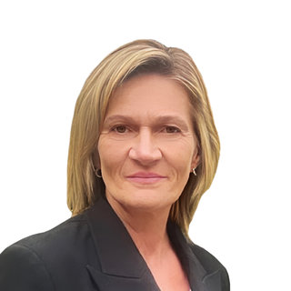Ein Porträt einer Frau mit blonden Haaren, die in einem schwarzen Blazer gekleidet ist. Sie lächelt freundlich und schaut direkt in die Kamera. Der Hintergrund ist einfarbig weiß.