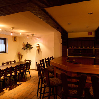 Ein gemütlicher Raum mit einem langen Tisch und mehreren Stühlen, die für ein Treffen oder eine Feier angeordnet sind. Im Hintergrund befindet sich eine Bar mit Holzregalen. Die Beleuchtung ist sanft und sorgt für eine einladende Atmosphäre.