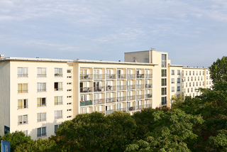 Ein mehrstöckiges Wohngebäude mit vielen Fenstern und Balkonen, umgeben von Bäumen. Der Himmel ist teilweise bewölkt.